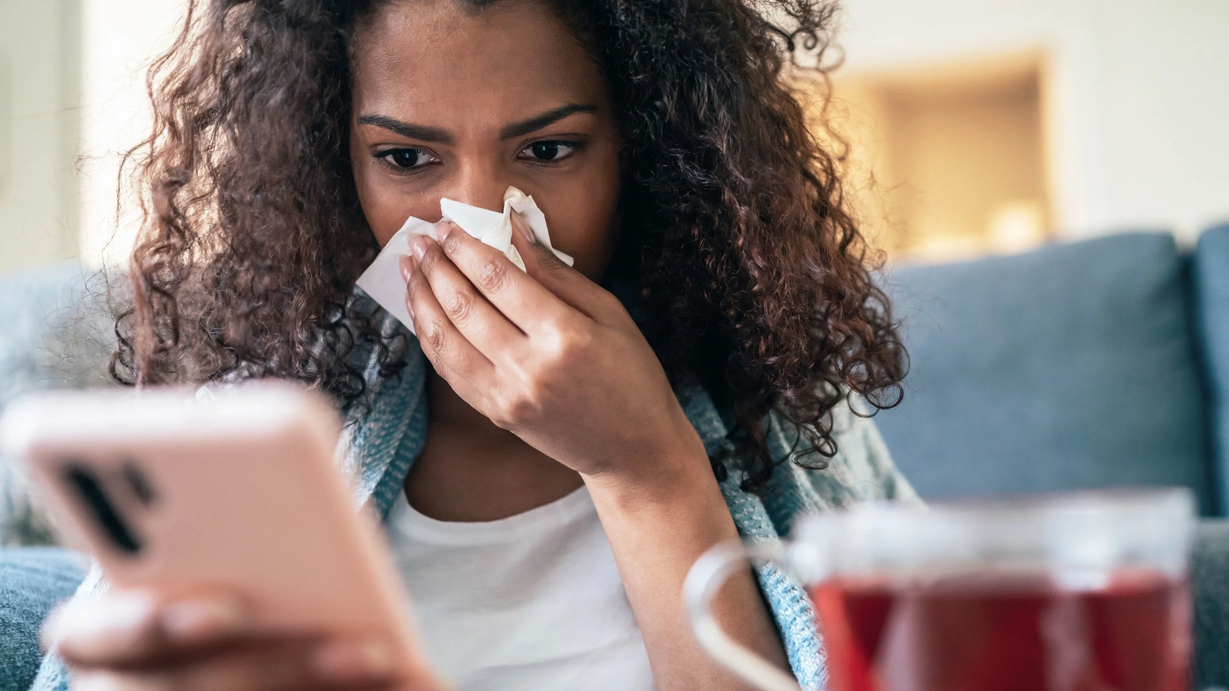 A person blowing their nose and looking at their phone.