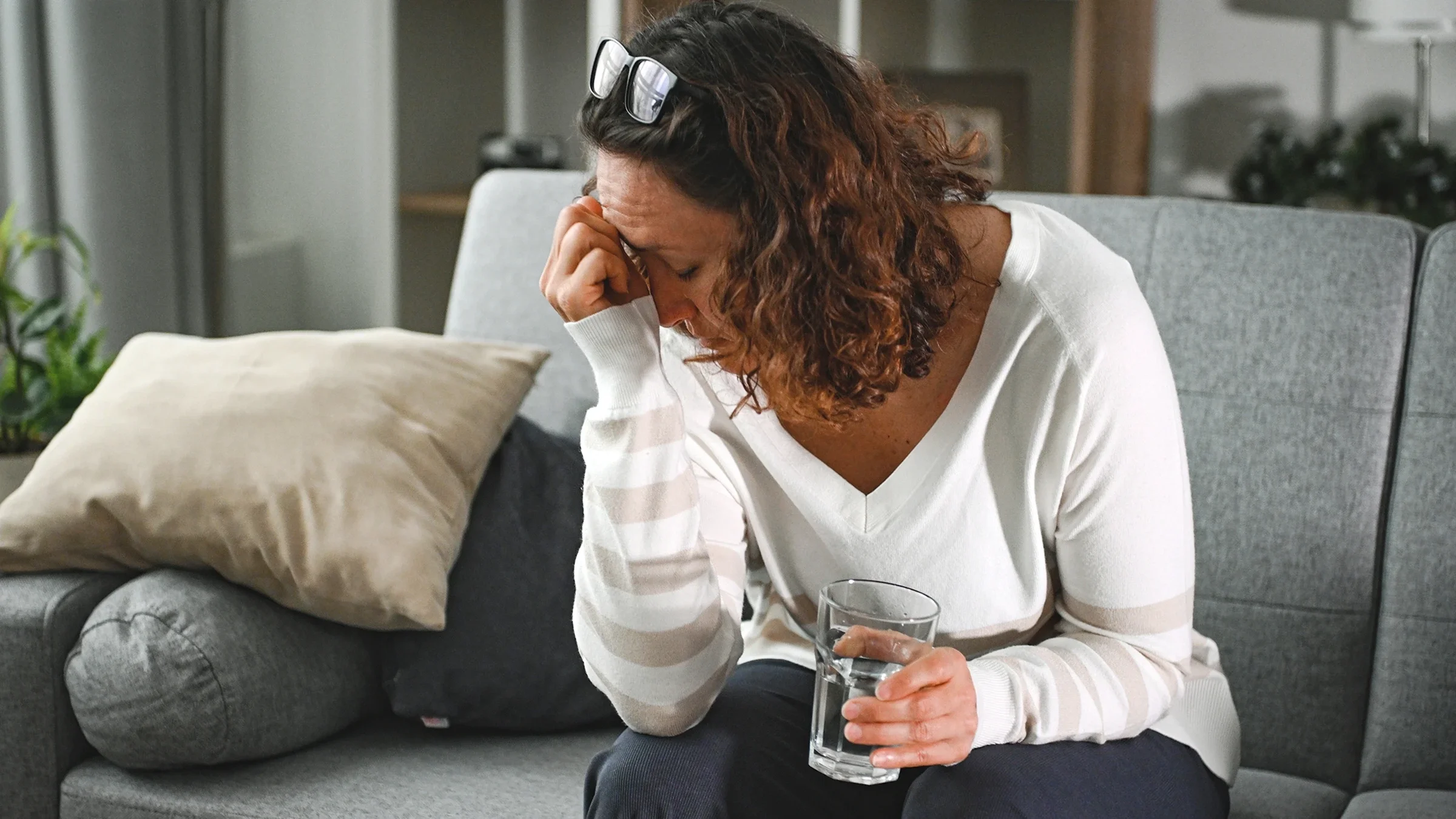 A woman with a headache drinks a glass of water.