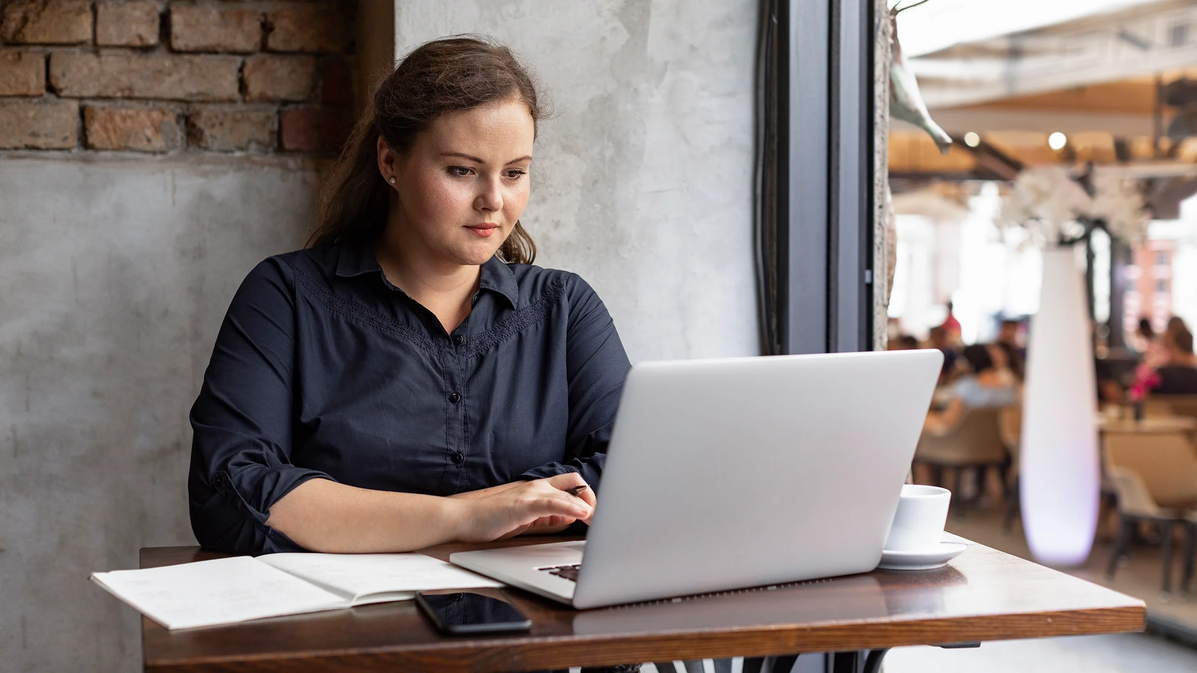 Young woman sitting at her laptop working in a coffee shop.