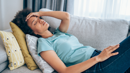 Woman with a fever laying down on the couch with her hand on her forehead.
VioletaStoimenova/E+ via Getty Images
