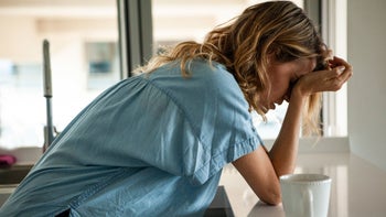 Headaches: woman with headache leaning on counter GettyImages 1321004522