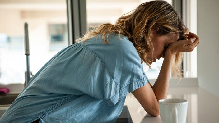 A woman with a headache is leaning on a counter.