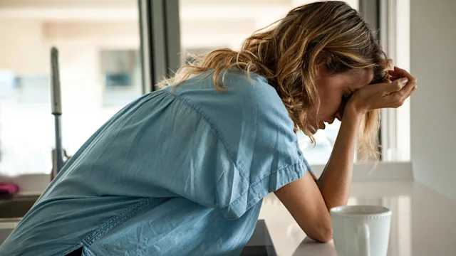 Headaches: woman with headache leaning on counter GettyImages 1321004522