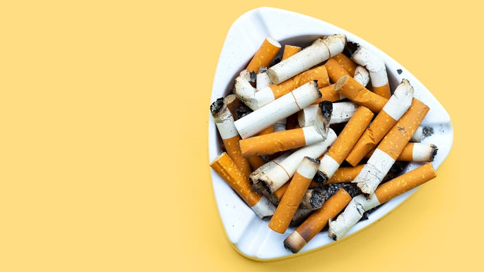 An ashtray full of cigarette butts is seen on a yellow background.