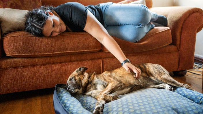 A woman is petting her dog while lying on a sofa.
