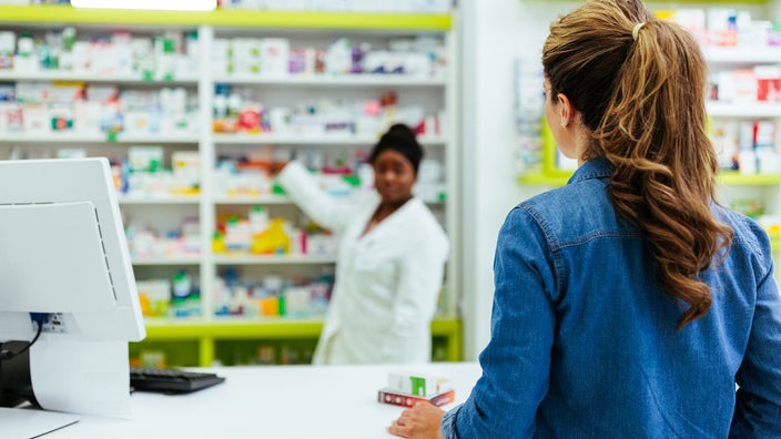 A pharmacist sells medication to a woman at the pharmacy counter.