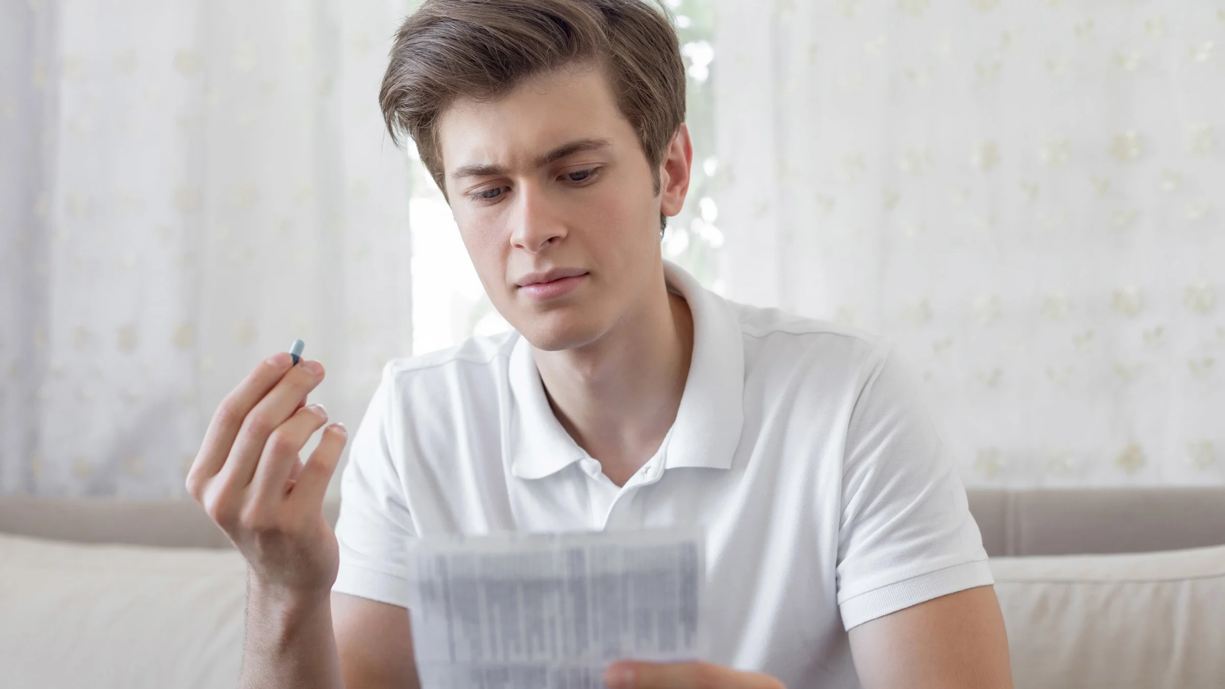 A person holding a pill and reading the instruction labels that came with it.