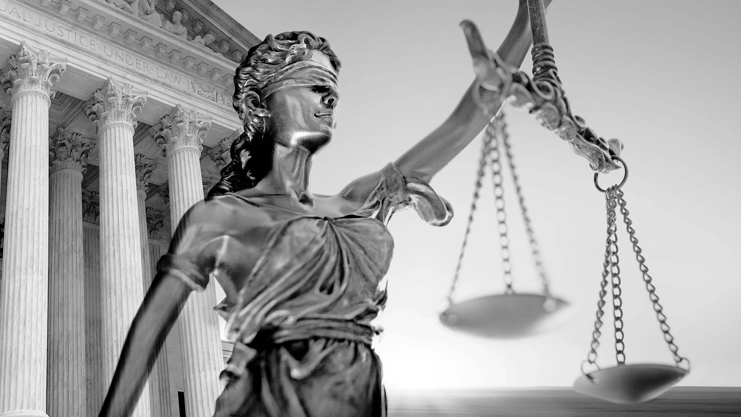 Black and white photo of a statue of Lady Justice holding the justice scales in front of the Supreme Court building.