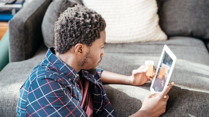 Young man sitting on the floor in front of the couch using his tablet and reviewing his medications.