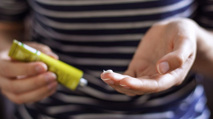 Close-up on a woman's hands putting a face ointment on her finger from a yellow-green tube.