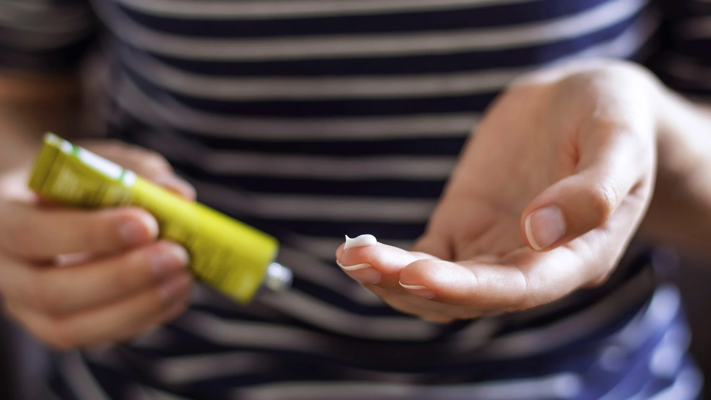 Close-up on a woman's hands putting a face ointment on her finger from a yellow-green tube.