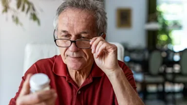 Senior man adjusting his glasses while he reads a pill bottle in his hand.
PIKSEL/iStock via Getty Images