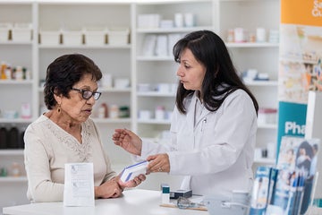 Elderly woman looking at a prescription box with her pharmacist at the counter.
