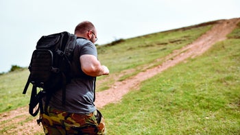 Health: Movement and exercise: man walking uphill with weighted backpack 1250423752
