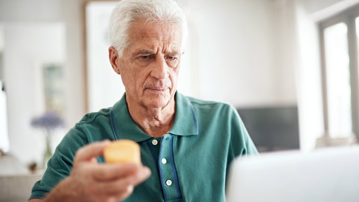 A man holding a pill bottle in front of a laptop.