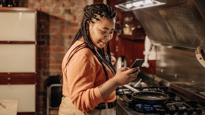 A woman looks at a recipe on her phone while preparing a meal in the kitchen.