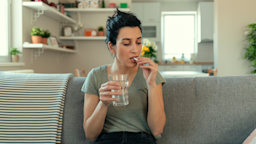 Woman on couch taking white pill.
PixelsEffect/E+ via Getty Images
