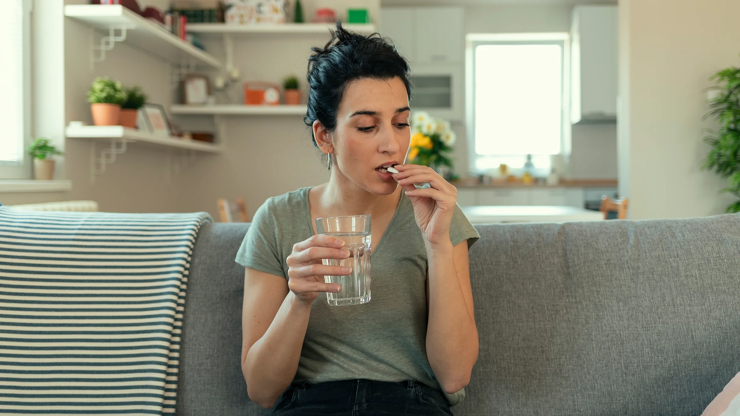 Woman on couch taking white pill.