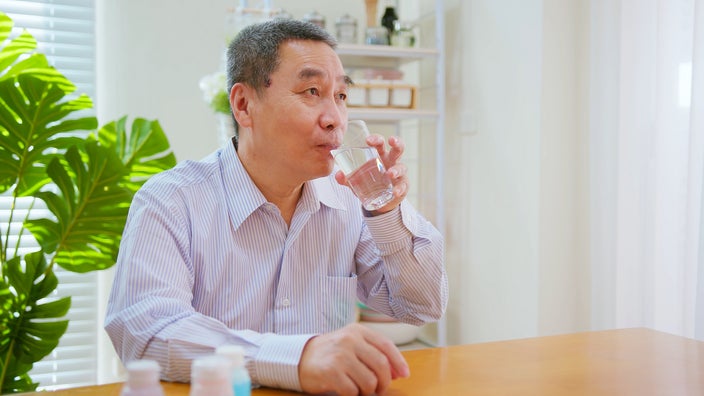 An older man takes medication with a glass of water.