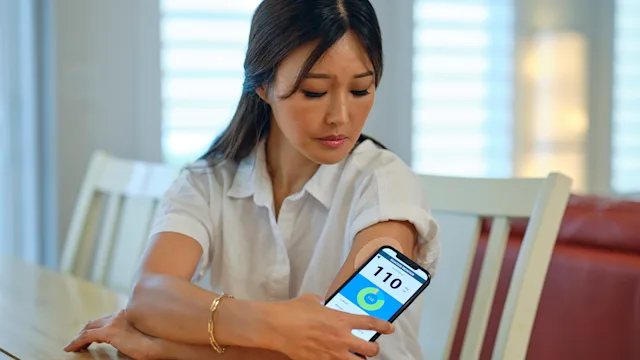 Diabetes: woman using continuous glucose monitor with smartphone 1413332880
