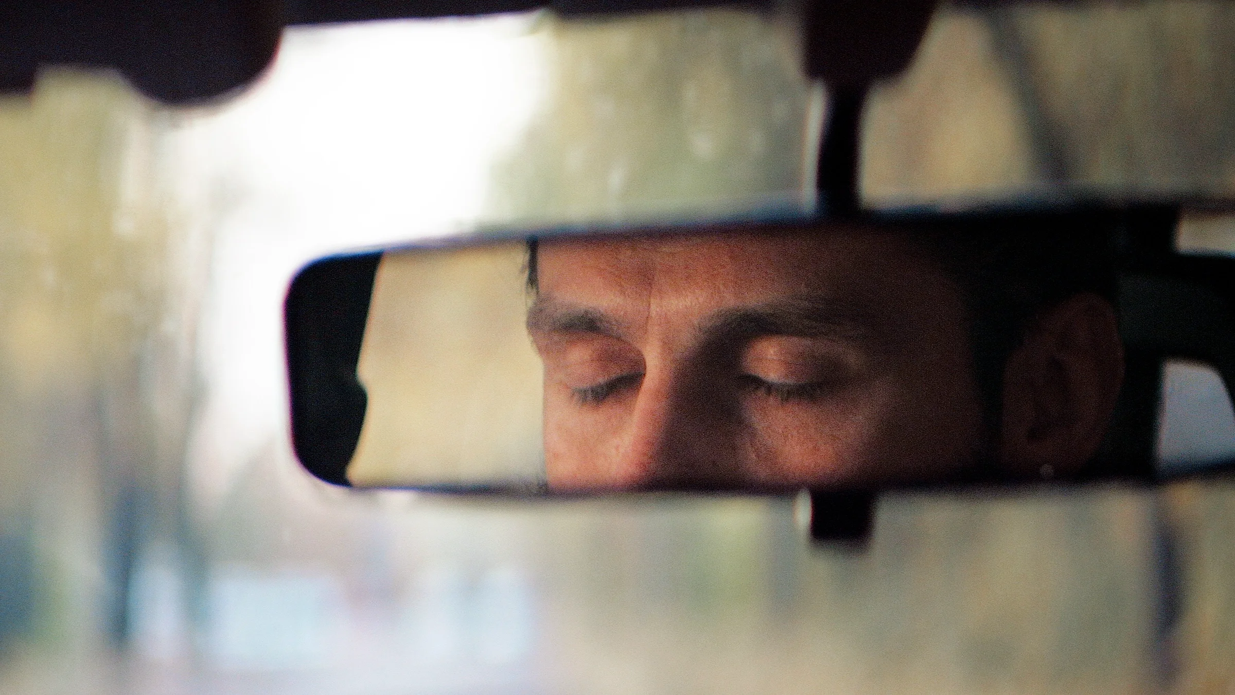 From the perspective of the rear view mirror, a person has their eyes closed.
