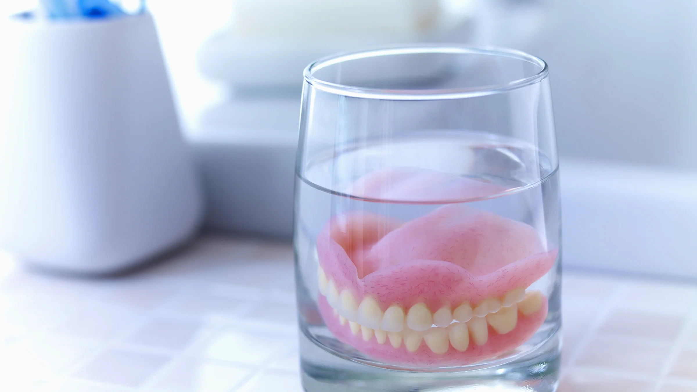 A close-up image shows dentures soaking in glass of water.