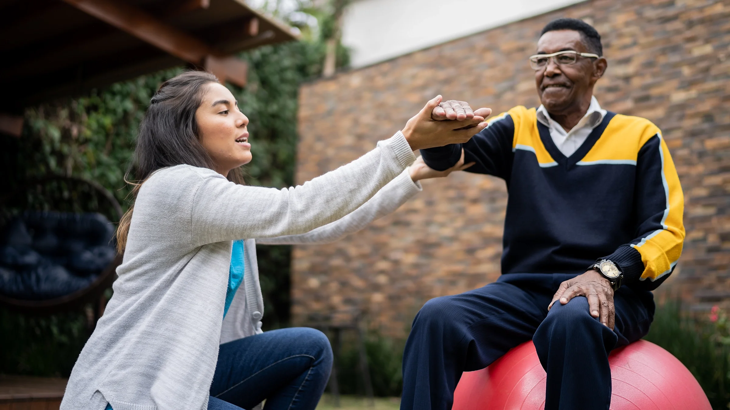 An older adult is doing physical therapy in the yard with his doctor.