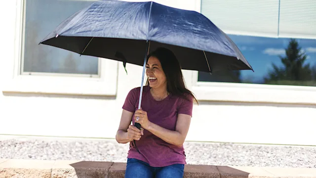 Dermatology: woman sitting under a umbrella for sun protection 1218851651