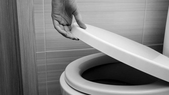 Black and white close-up of a hand lifting up toilet seat.