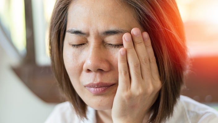 Close-up of a woman with her eyes closed and rubbing her temple. She looks like she has a severe headache.