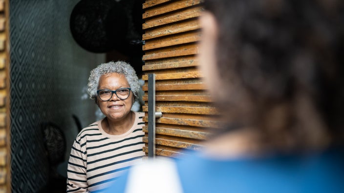 A senior woman opening their front door for a visitor.