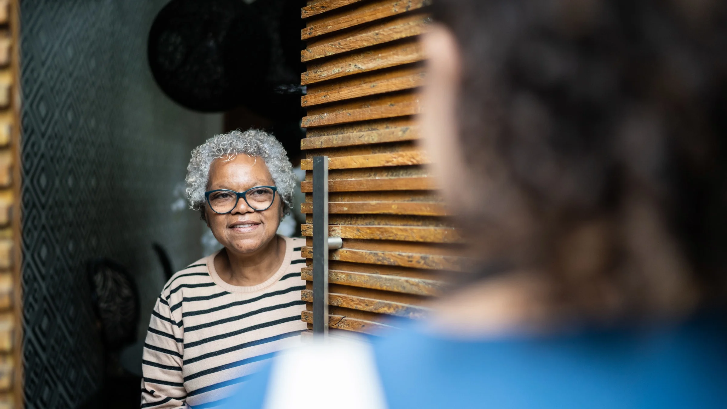 A senior woman opening their front door for a visitor.