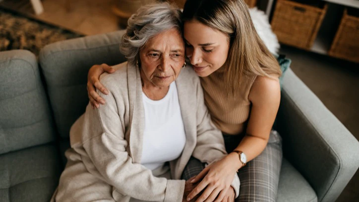 Overhead shot of a young woman side hugging her grandmother on the couch.