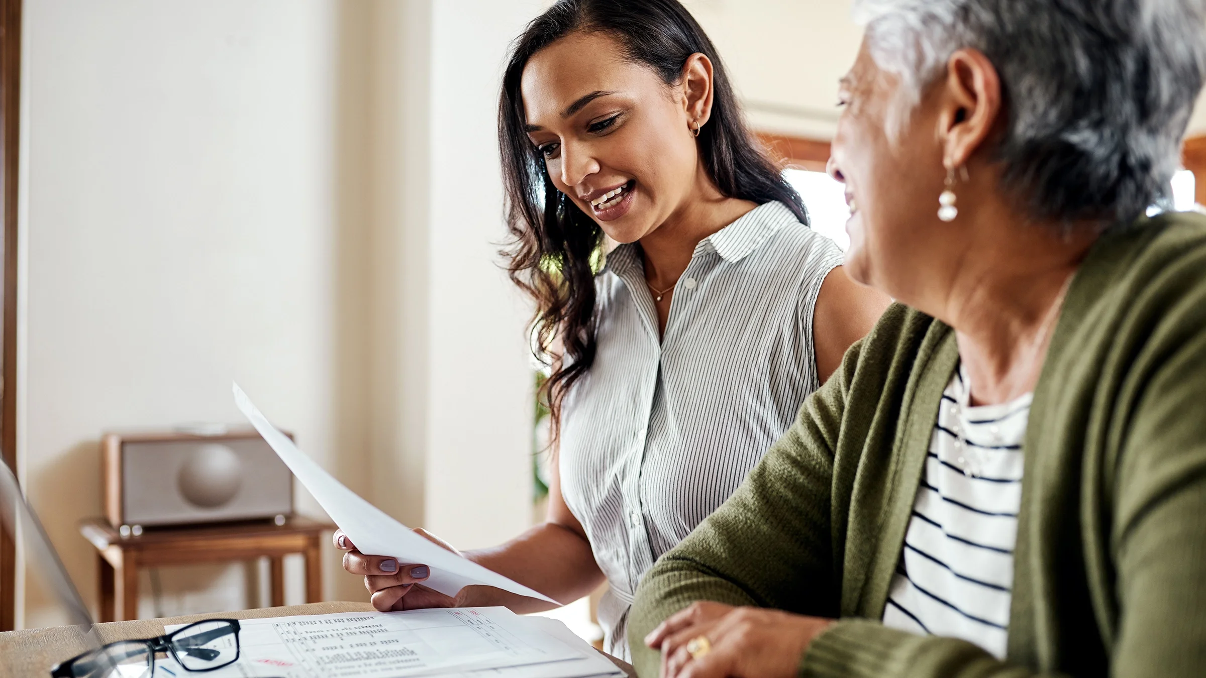 A younger woman helps a senior woman with paperwork.