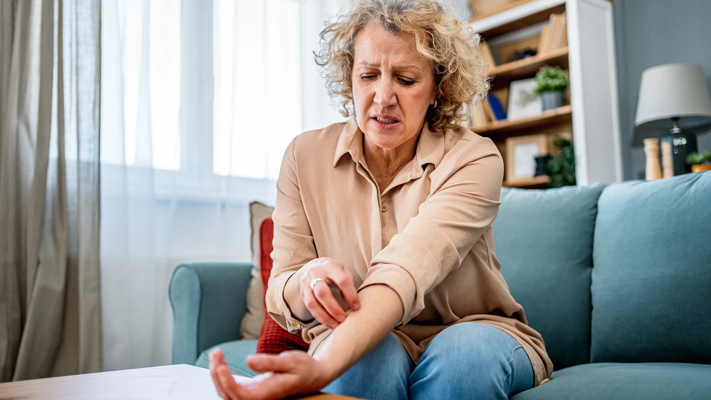 A woman scratches her forearm as she sits on a couch.