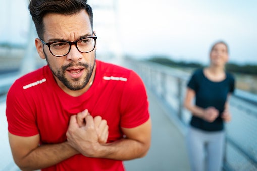Young man in workout shirt clenching chest in pain.