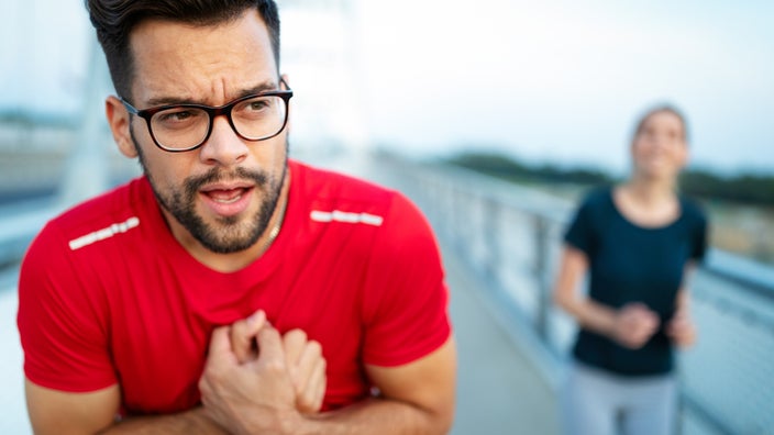 Young man in workout shirt clenching chest in pain.