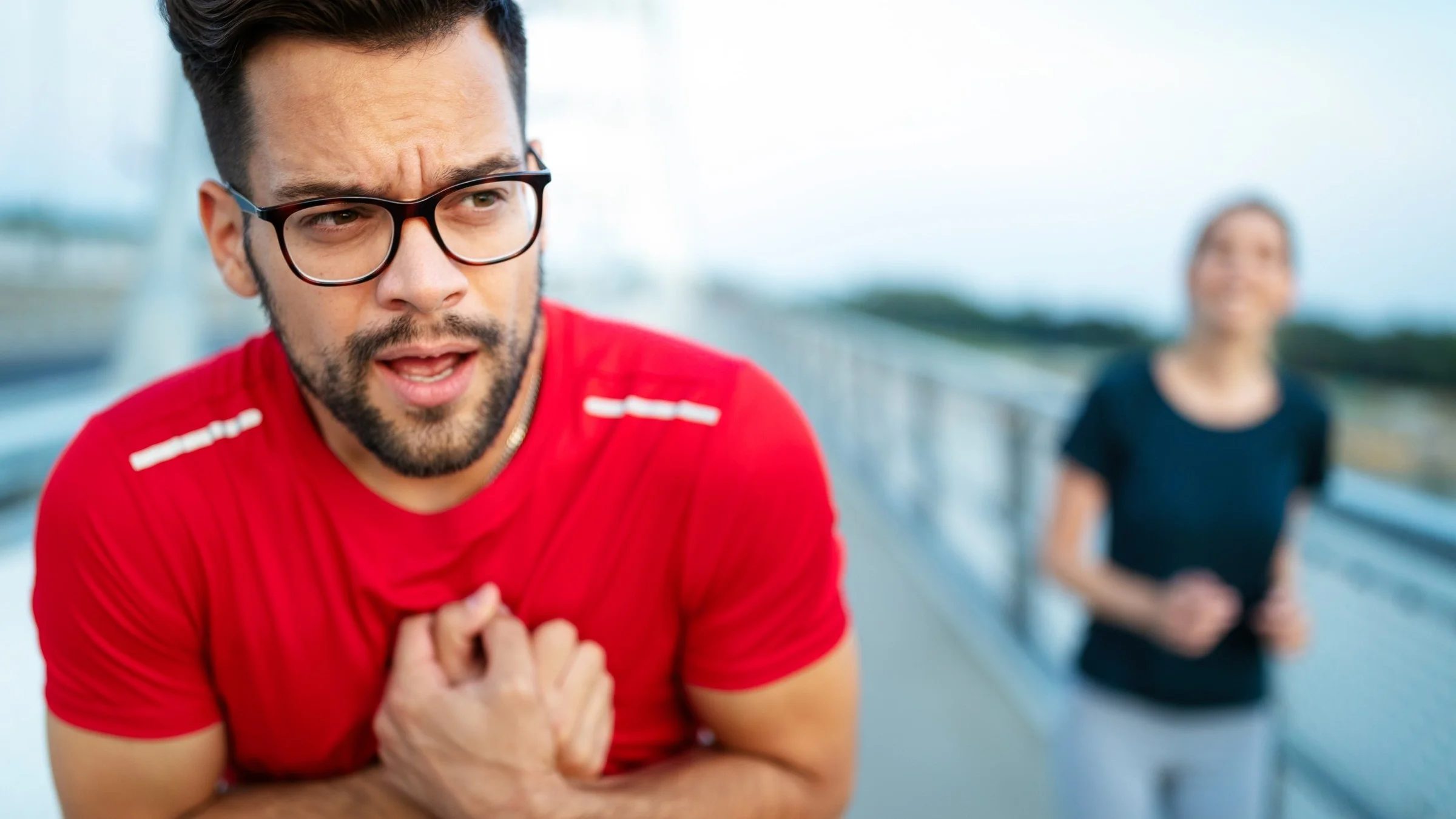 Young man in workout shirt clenching chest in pain.