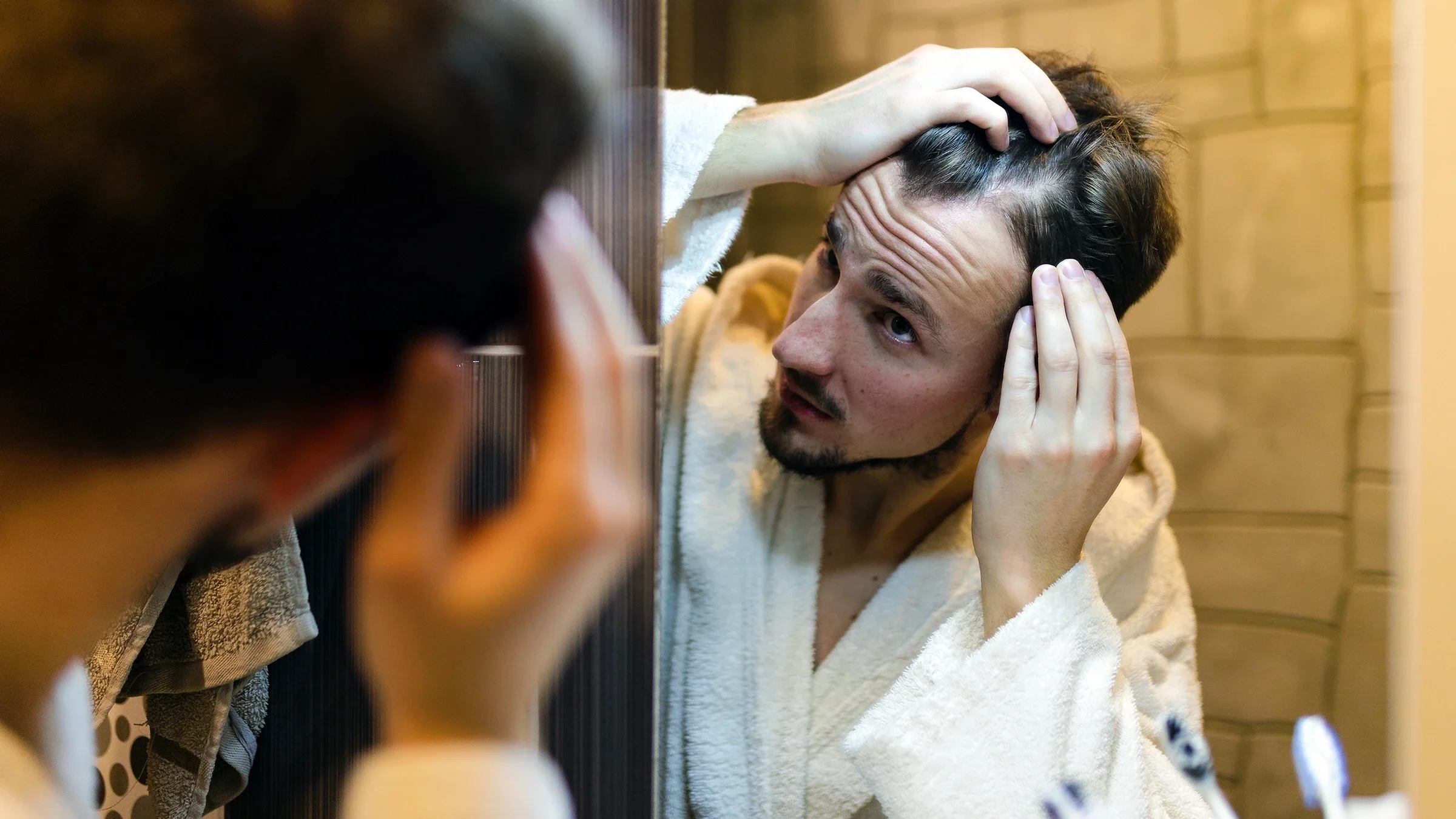 A man is checking his hairline in the mirror.