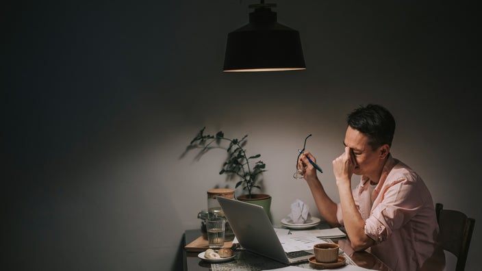 A person sitting at their dining table, looking stressed out over their bills.