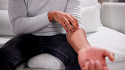 A man scratches his forearm while sitting on the couch.
AndreyPopov/iStock via Getty Images Plus 