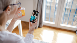 Woman holds a bottle of medicine in her hand during a telemedicine appointment.
blackCAT/E+ via Getty Images