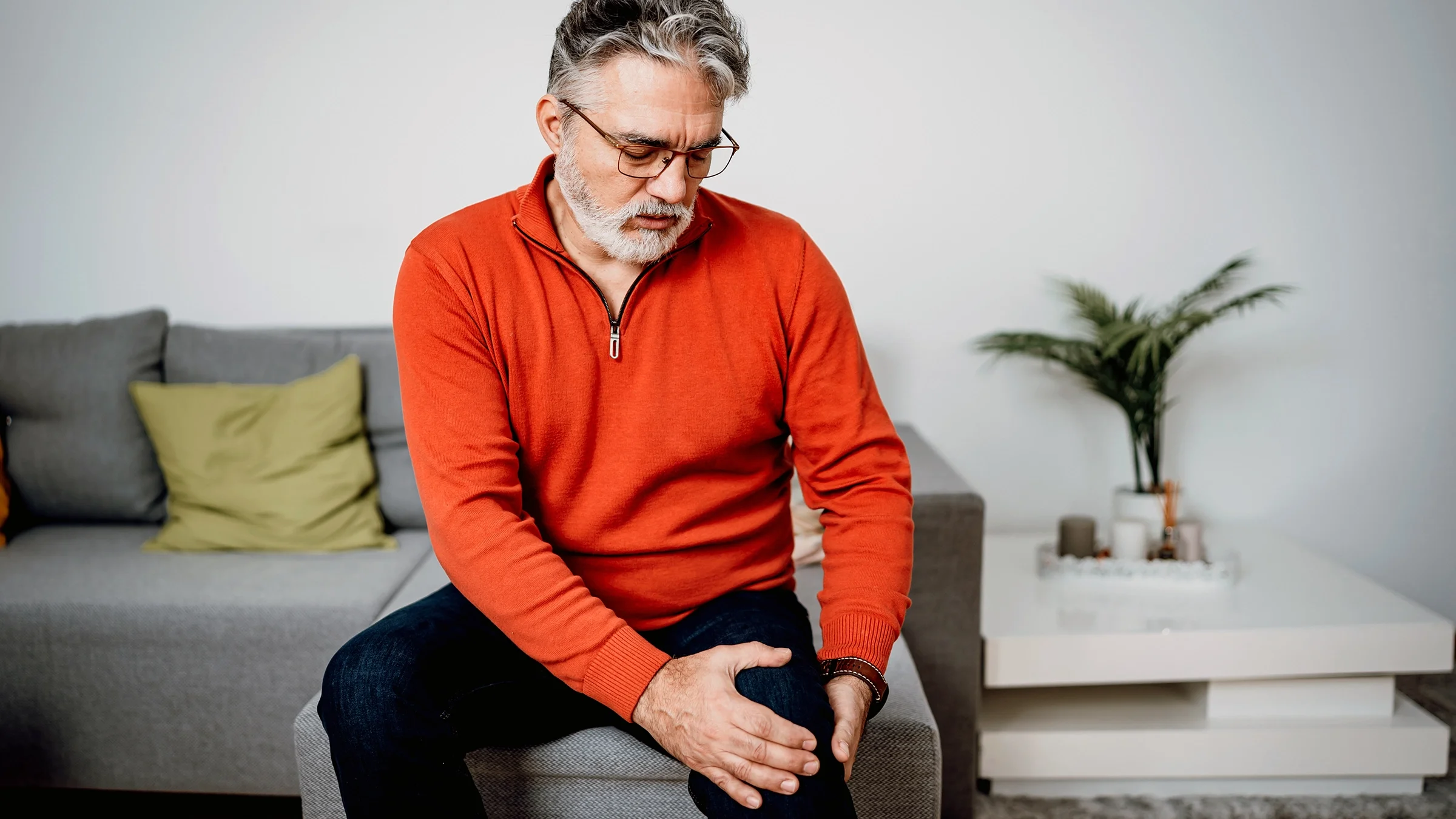 Man sitting on the sofa and holding his knee