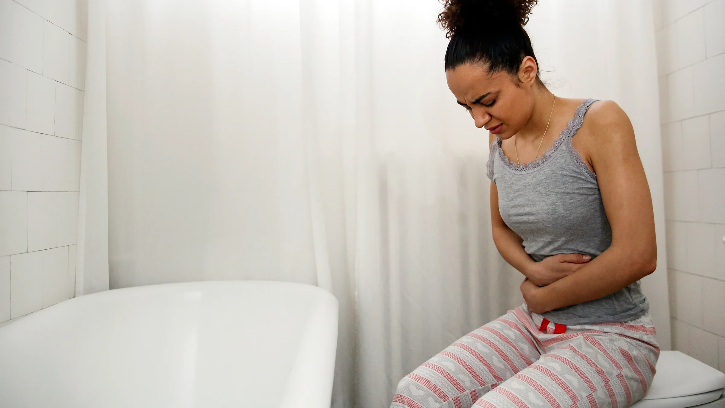 A woman with stomach pain sits in the bathroom. Probiotics can help with gut health, but they can also cause side effects like constipation.