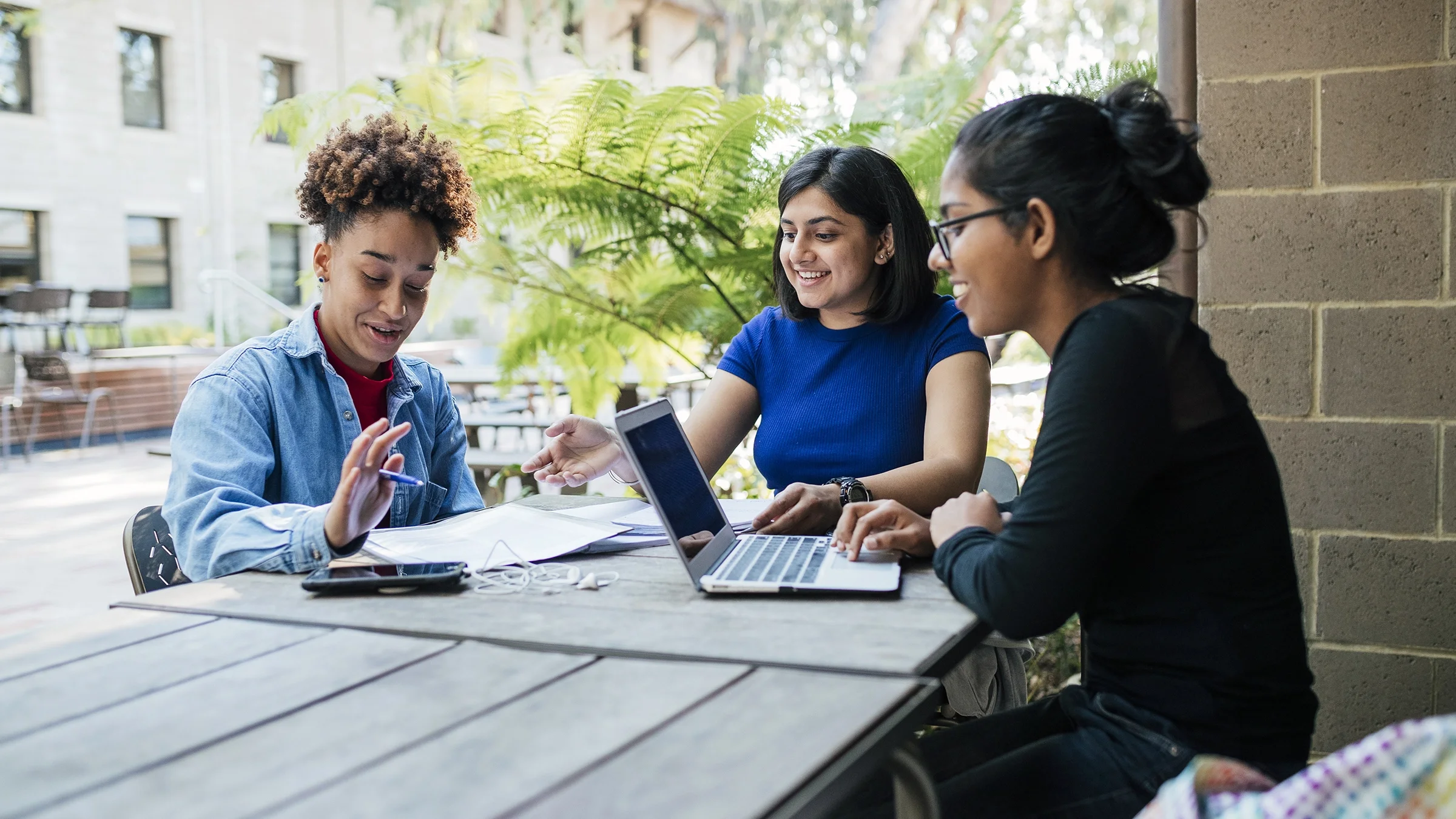 A group of college students studies at an outdoor table.