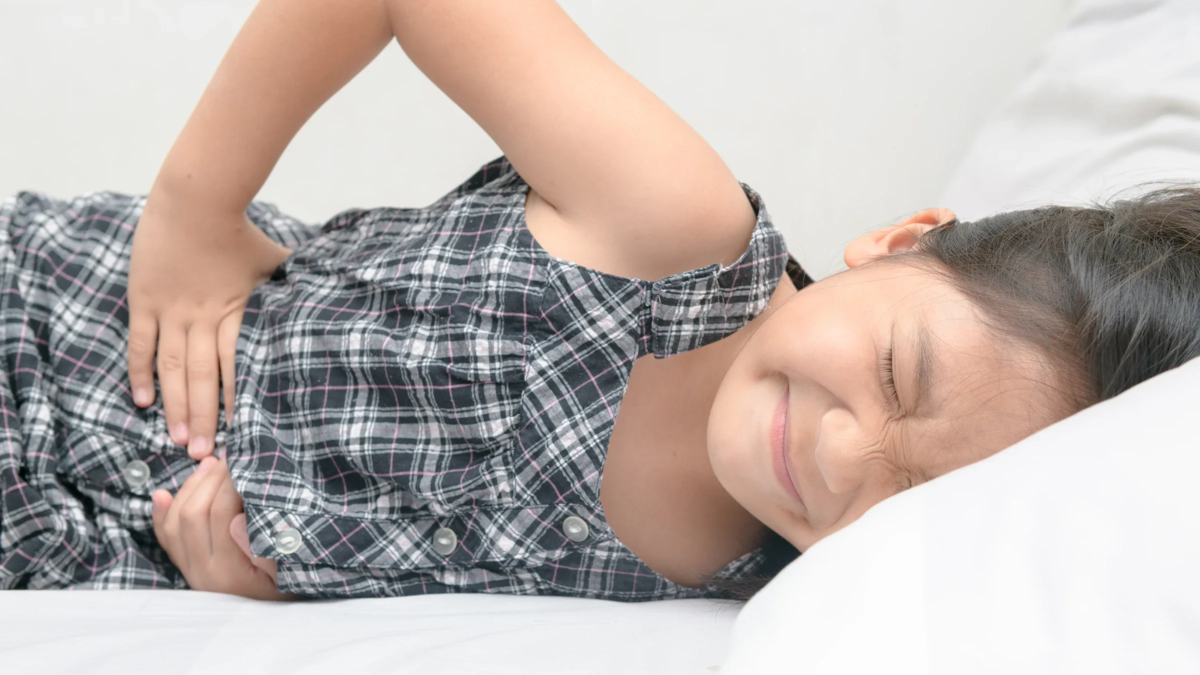 Close-up of a young girl lying down with a stomach ache. She is wincing in pain.
kwanchaichaiudom/iStock via Getty Images