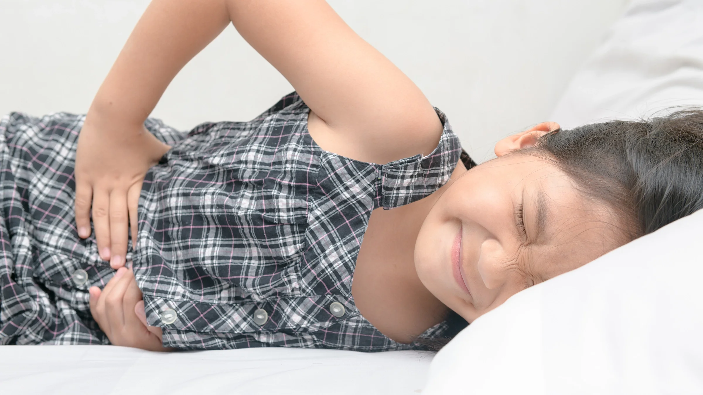 Close-up of a young girl lying down with a stomach ache. She is wincing in pain.
