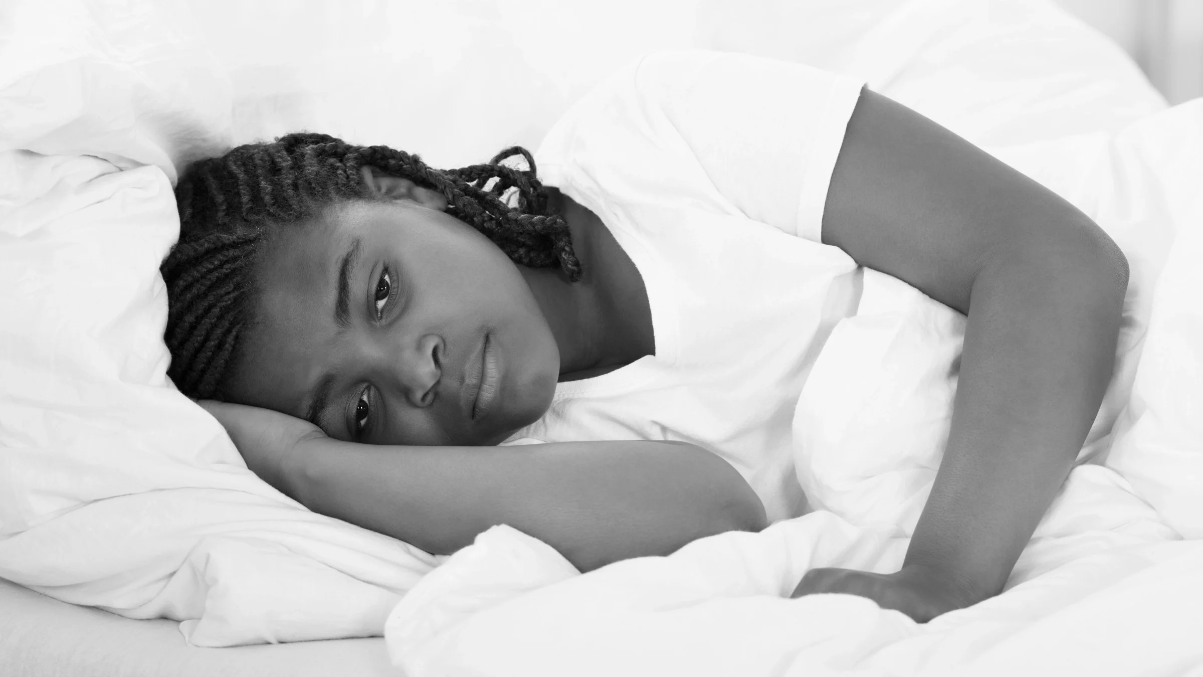 Black and white image of a young girl trying to sleep in her bed but doesn't look tired.