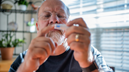 An older man with glasses and a beard checks his blood sugar. 
grandriver/E+ via Getty Images