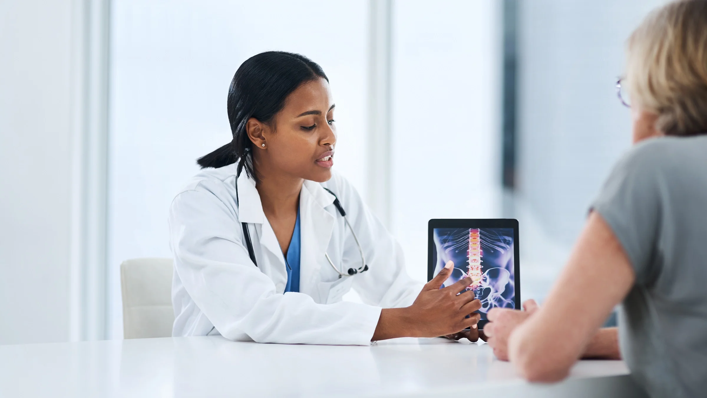 A doctor shows a patient a spinal cord X-ray on a tablet.